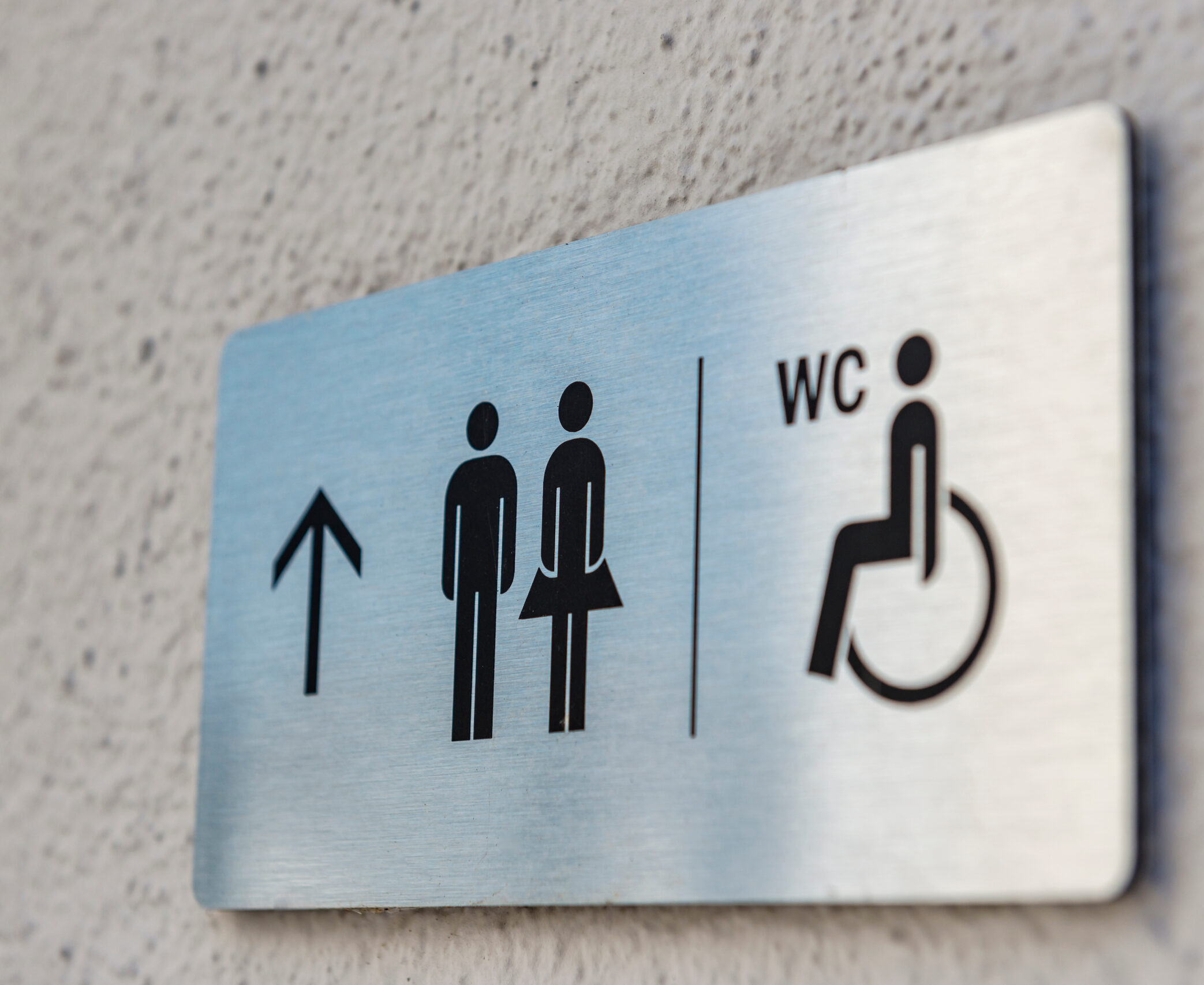 Men and women accessible restroom sign on a white wall with wayfinding arrow